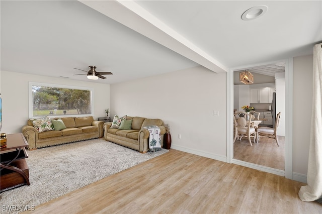 living area with a ceiling fan, beamed ceiling, light wood-style flooring, and baseboards