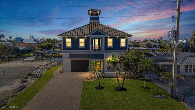 raised beach house featuring a front lawn, metal roof, decorative driveway, an attached garage, and a standing seam roof