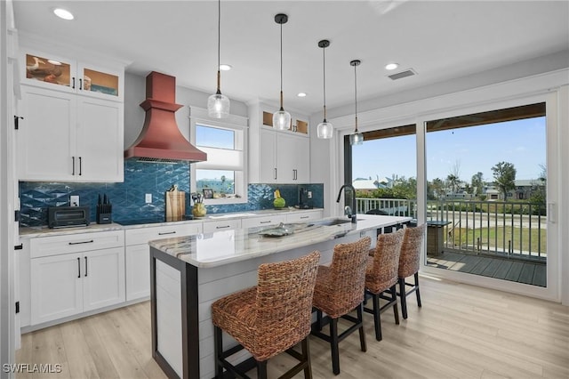 kitchen featuring visible vents, a sink, custom range hood, light wood-style floors, and black electric cooktop