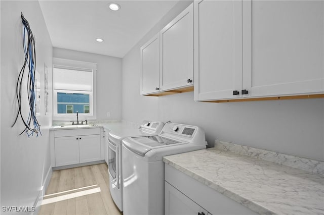 clothes washing area with light wood finished floors, washer and clothes dryer, recessed lighting, cabinet space, and a sink