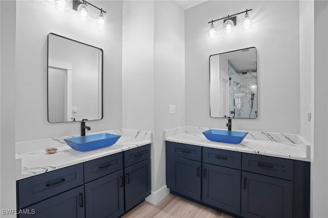 full bathroom with wood finished floors, two vanities, walk in shower, and a sink