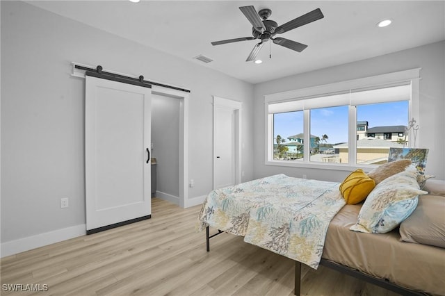 bedroom featuring visible vents, baseboards, light wood-type flooring, a barn door, and recessed lighting