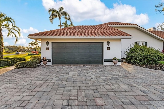 view of front of home featuring decorative driveway, a tiled roof, an attached garage, and stucco siding