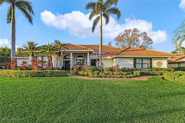 mediterranean / spanish home with a tile roof, a front lawn, and stucco siding