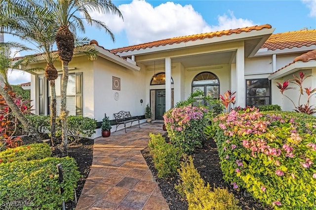 entrance to property featuring covered porch, a tiled roof, and stucco siding