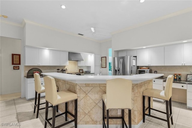 kitchen with stainless steel appliances, wall chimney range hood, a breakfast bar, and crown molding