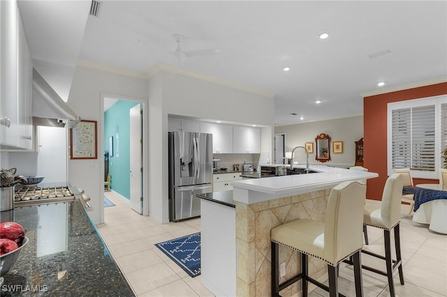 kitchen featuring a breakfast bar, stainless steel refrigerator with ice dispenser, light tile patterned floors, ornamental molding, and a sink