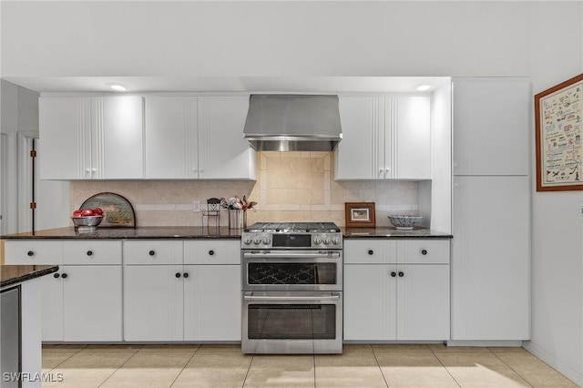 kitchen featuring white cabinets, wall chimney exhaust hood, range with two ovens, and backsplash