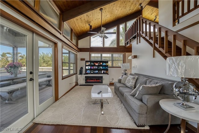 living room featuring beamed ceiling, wooden ceiling, a glass covered fireplace, and a healthy amount of sunlight