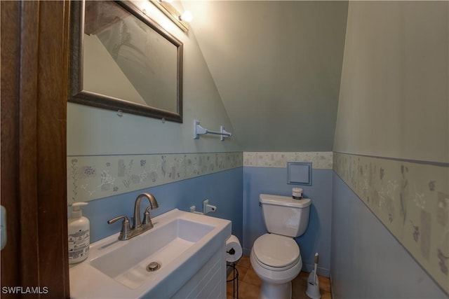 half bath with a wainscoted wall, lofted ceiling, toilet, vanity, and tile patterned flooring