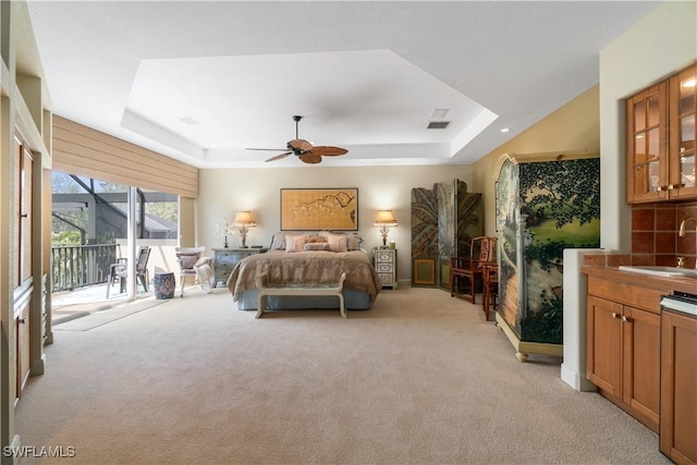 bedroom featuring access to exterior, a raised ceiling, a sink, and light colored carpet