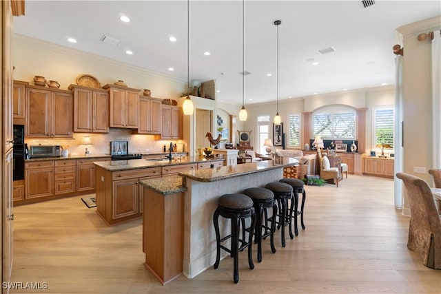 kitchen featuring light wood finished floors, tasteful backsplash, brown cabinetry, a breakfast bar area, and a large island with sink