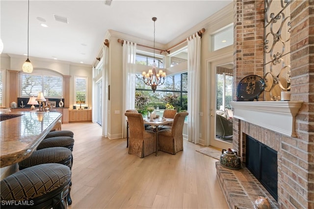 dining room with a fireplace, visible vents, ornamental molding, a chandelier, and light wood-type flooring