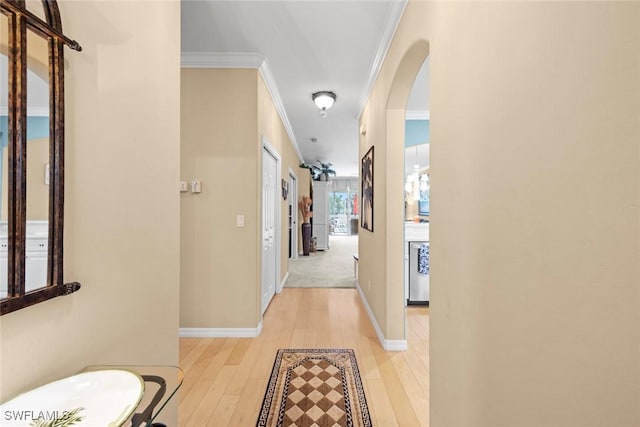 hall featuring ornamental molding, arched walkways, baseboards, and light wood finished floors