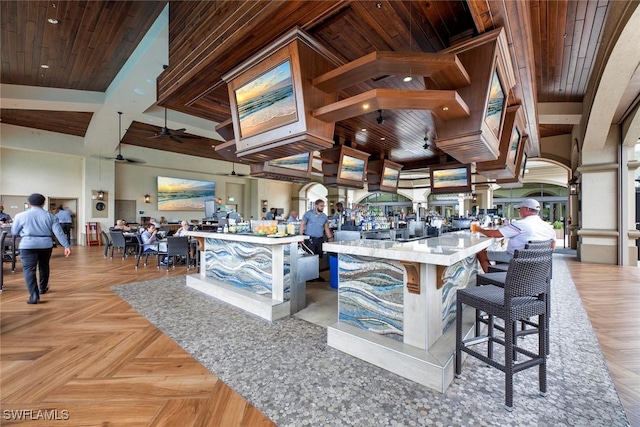 kitchen featuring a ceiling fan, open floor plan, wooden ceiling, and a towering ceiling