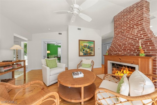 living room featuring a ceiling fan, wood finished floors, visible vents, lofted ceiling, and a brick fireplace