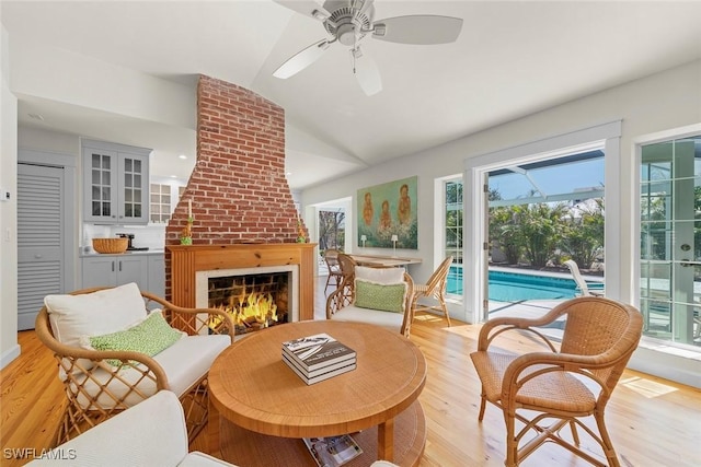 living area with light wood-type flooring, lofted ceiling, a brick fireplace, and visible vents