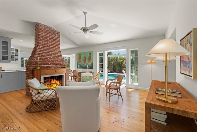 living area featuring ceiling fan, a fireplace, light wood-style floors, and vaulted ceiling