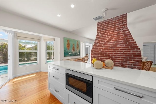 kitchen with stainless steel microwave, visible vents, light countertops, and light wood finished floors