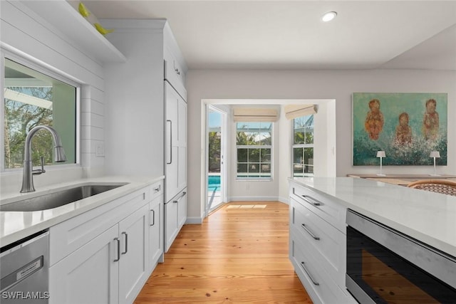 kitchen featuring a sink, white cabinetry, stainless steel appliances, light wood-style floors, and light countertops