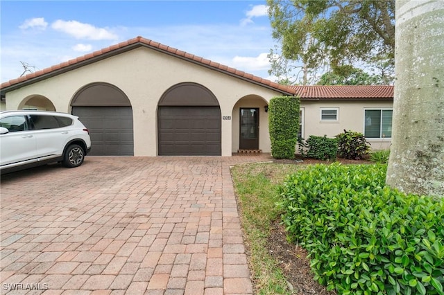 mediterranean / spanish-style house featuring an attached garage, a tiled roof, decorative driveway, and stucco siding