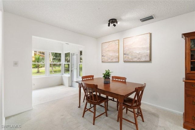 dining room with light carpet, baseboards, visible vents, and a textured ceiling