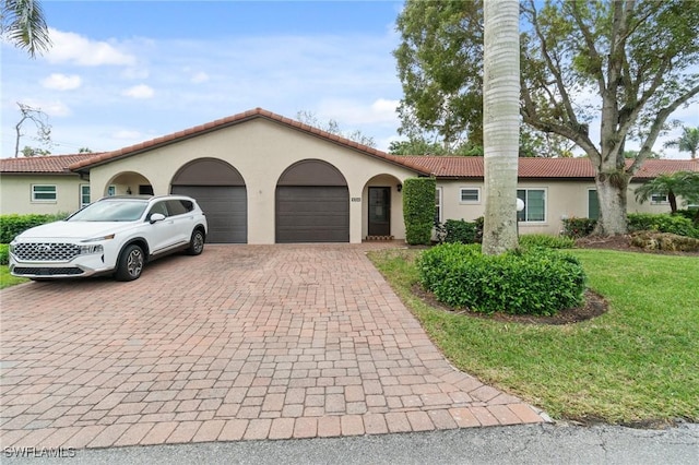 mediterranean / spanish-style home with an attached garage, a tile roof, decorative driveway, and stucco siding