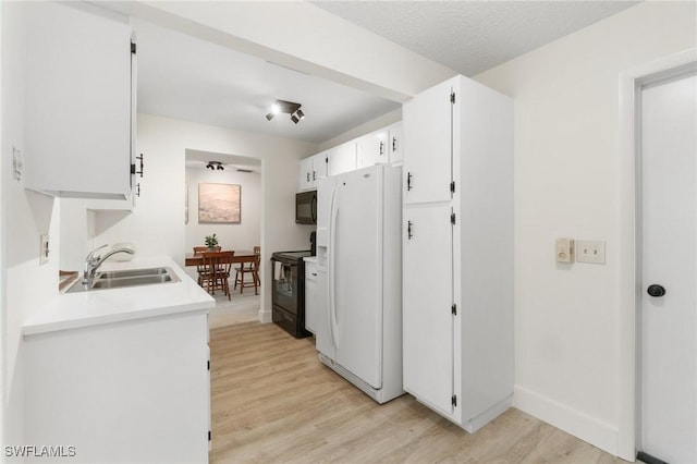 kitchen with white cabinets, light wood-style floors, light countertops, black appliances, and a sink