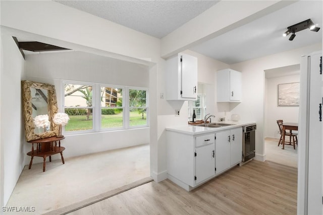 kitchen with a sink, white cabinets, black dishwasher, light countertops, and light wood finished floors