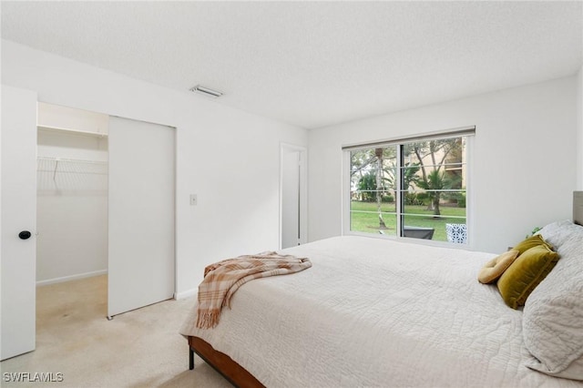 bedroom featuring light carpet, visible vents, a spacious closet, a textured ceiling, and a closet