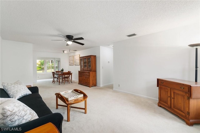 living room with light colored carpet, ceiling fan, a textured ceiling, and baseboards