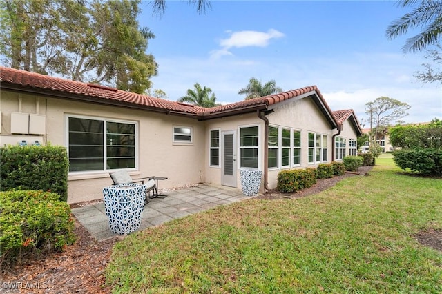 back of property with a tiled roof, a yard, a patio, and stucco siding