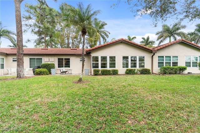 rear view of house with a tile roof, a lawn, and stucco siding