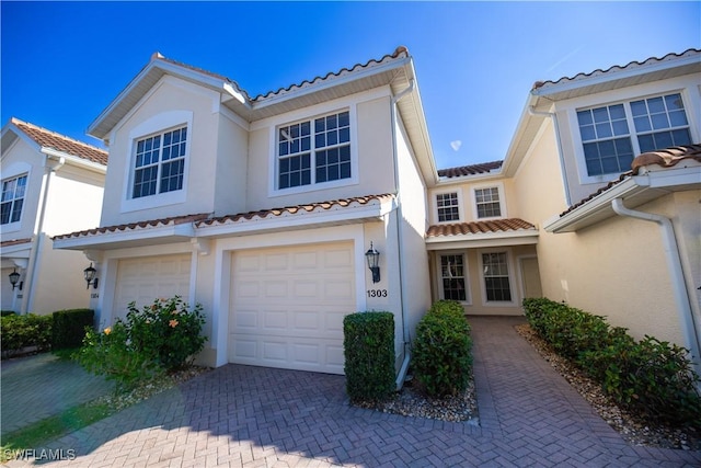 mediterranean / spanish house featuring an attached garage, a tiled roof, decorative driveway, and stucco siding