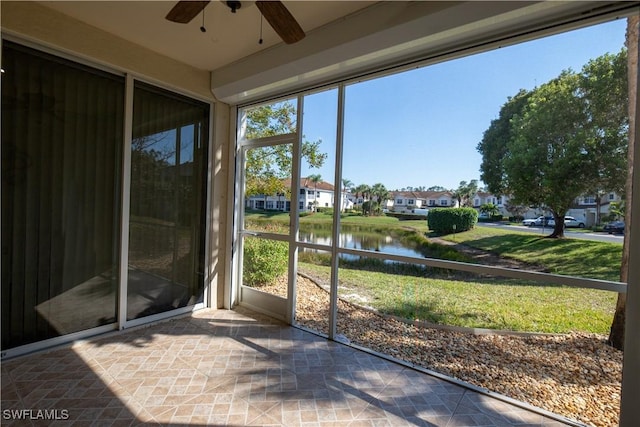 unfurnished sunroom featuring a ceiling fan, a residential view, and a water view