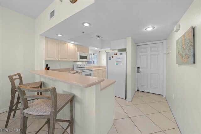 kitchen with white appliances, light tile patterned floors, a peninsula, light countertops, and a kitchen bar