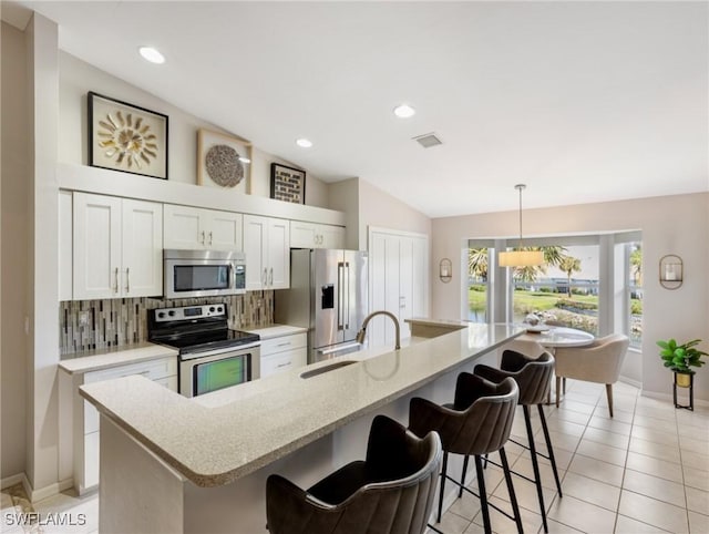 kitchen with lofted ceiling, a breakfast bar, a sink, appliances with stainless steel finishes, and tasteful backsplash