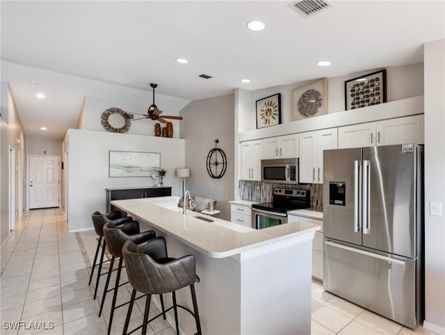 kitchen featuring a center island with sink, visible vents, white cabinets, appliances with stainless steel finishes, and a breakfast bar area