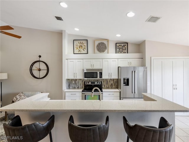 kitchen with a kitchen bar, appliances with stainless steel finishes, vaulted ceiling, and backsplash