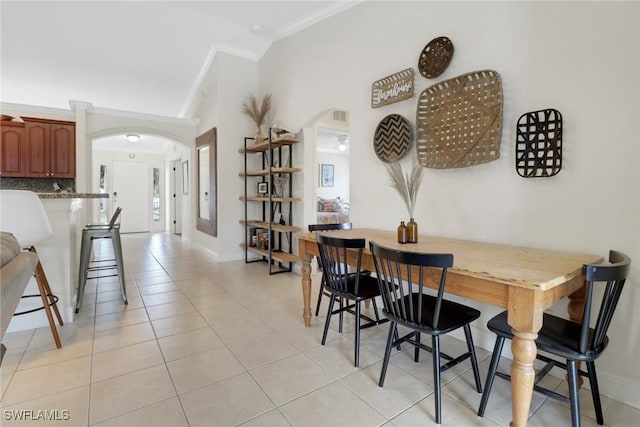 dining area featuring arched walkways, ornamental molding, vaulted ceiling, and light tile patterned flooring