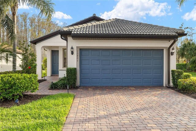 ranch-style home featuring decorative driveway, an attached garage, a tile roof, and stucco siding