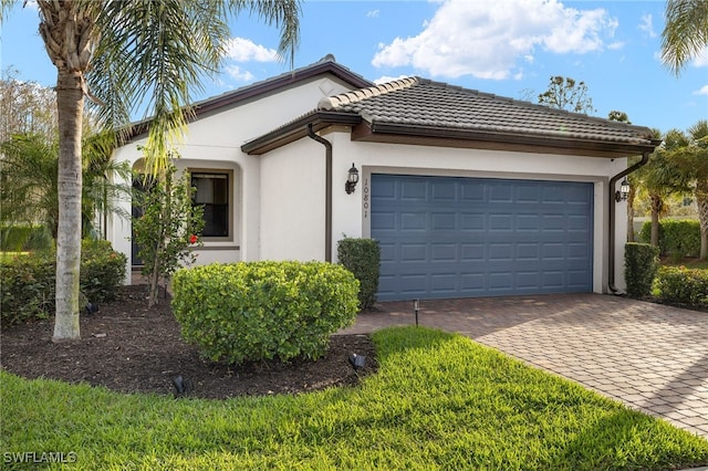 single story home with a garage, decorative driveway, a tiled roof, and stucco siding