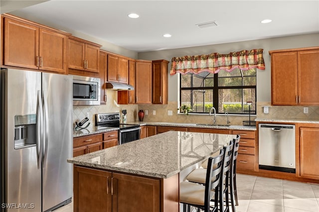 kitchen featuring a breakfast bar, brown cabinets, stainless steel appliances, a sink, and under cabinet range hood