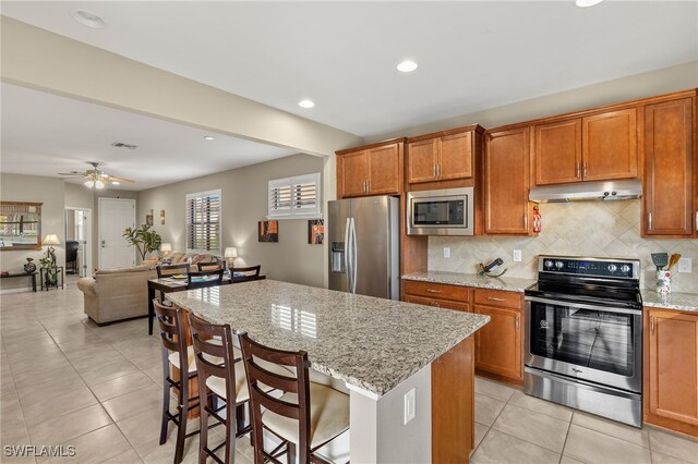 kitchen with under cabinet range hood, tasteful backsplash, stainless steel appliances, and brown cabinetry