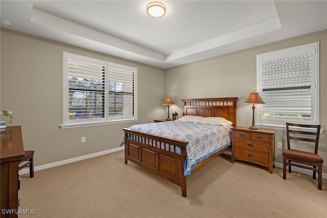 bedroom with light carpet, multiple windows, baseboards, and a raised ceiling