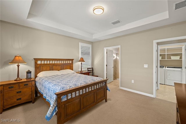 bedroom with washing machine and dryer, a raised ceiling, visible vents, and light carpet