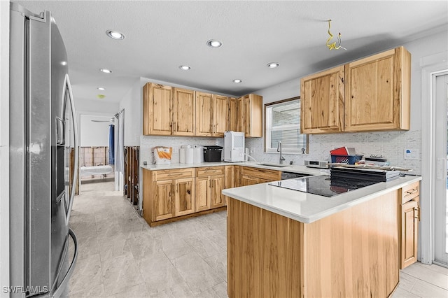 kitchen with tasteful backsplash, light countertops, a sink, stainless steel fridge, and a peninsula