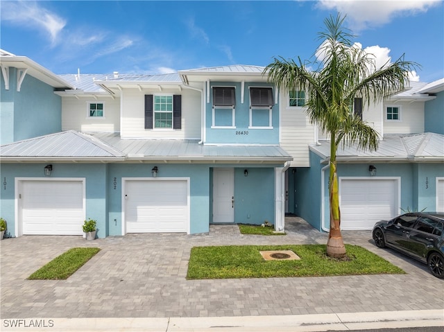 townhome / multi-family property with metal roof, driveway, an attached garage, and stucco siding