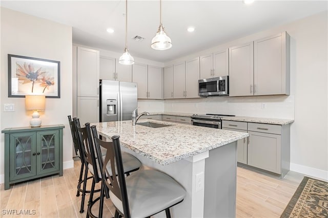 kitchen with light stone counters, decorative backsplash, appliances with stainless steel finishes, light wood-style floors, and a sink