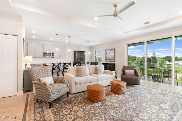 living area with recessed lighting, a ceiling fan, visible vents, light wood finished floors, and a tray ceiling